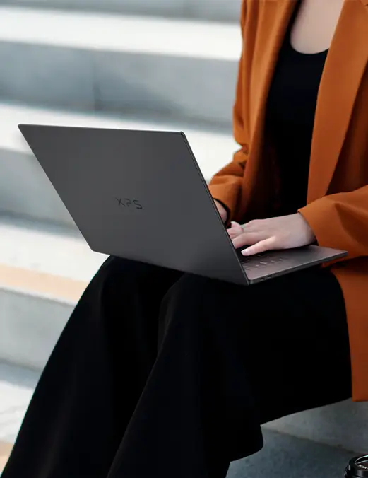 Kobieta pracująca na laptopie Dell XPS 16 siedząc na schodach