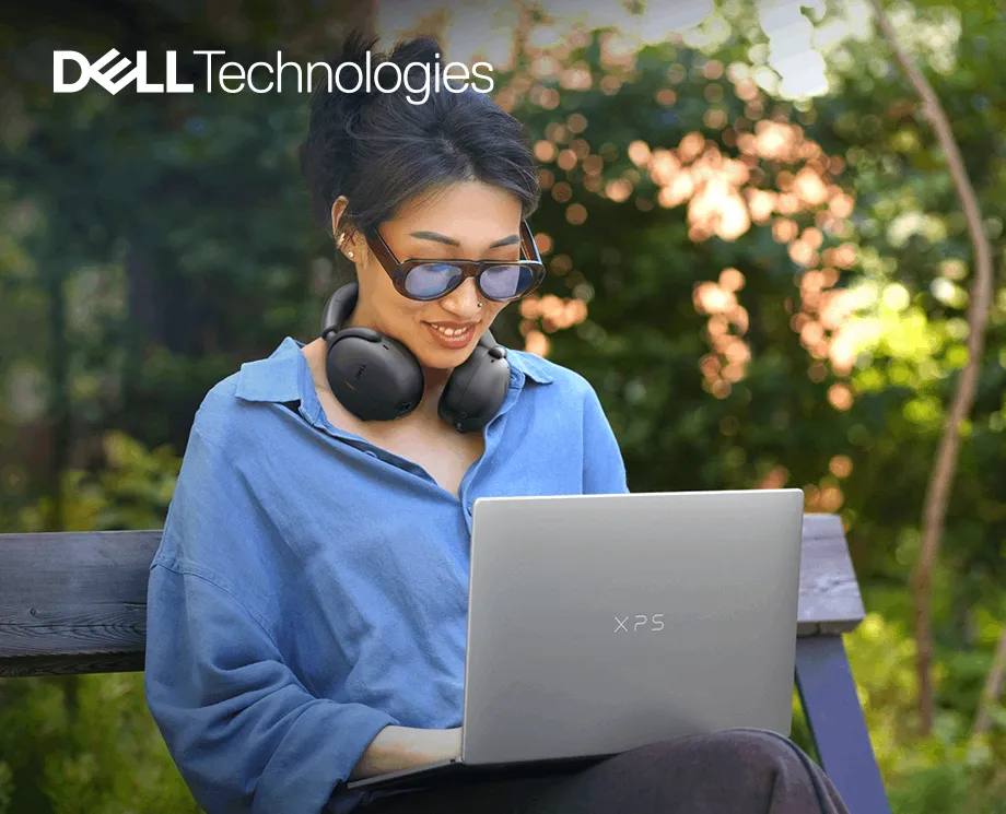 Logo Dell Technologies, a pod nim młoda kobieta ze słuchawkami na szyi pracująca na laptopie XPS 13 na ławce w ogrodzie